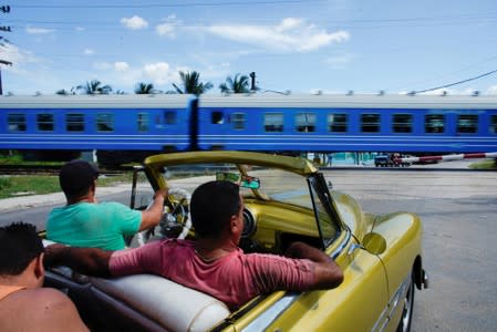 People wait in a vintage car as Cuba's Chinese-made first new train passenger cars move after departing from La Coubre train station in Havana