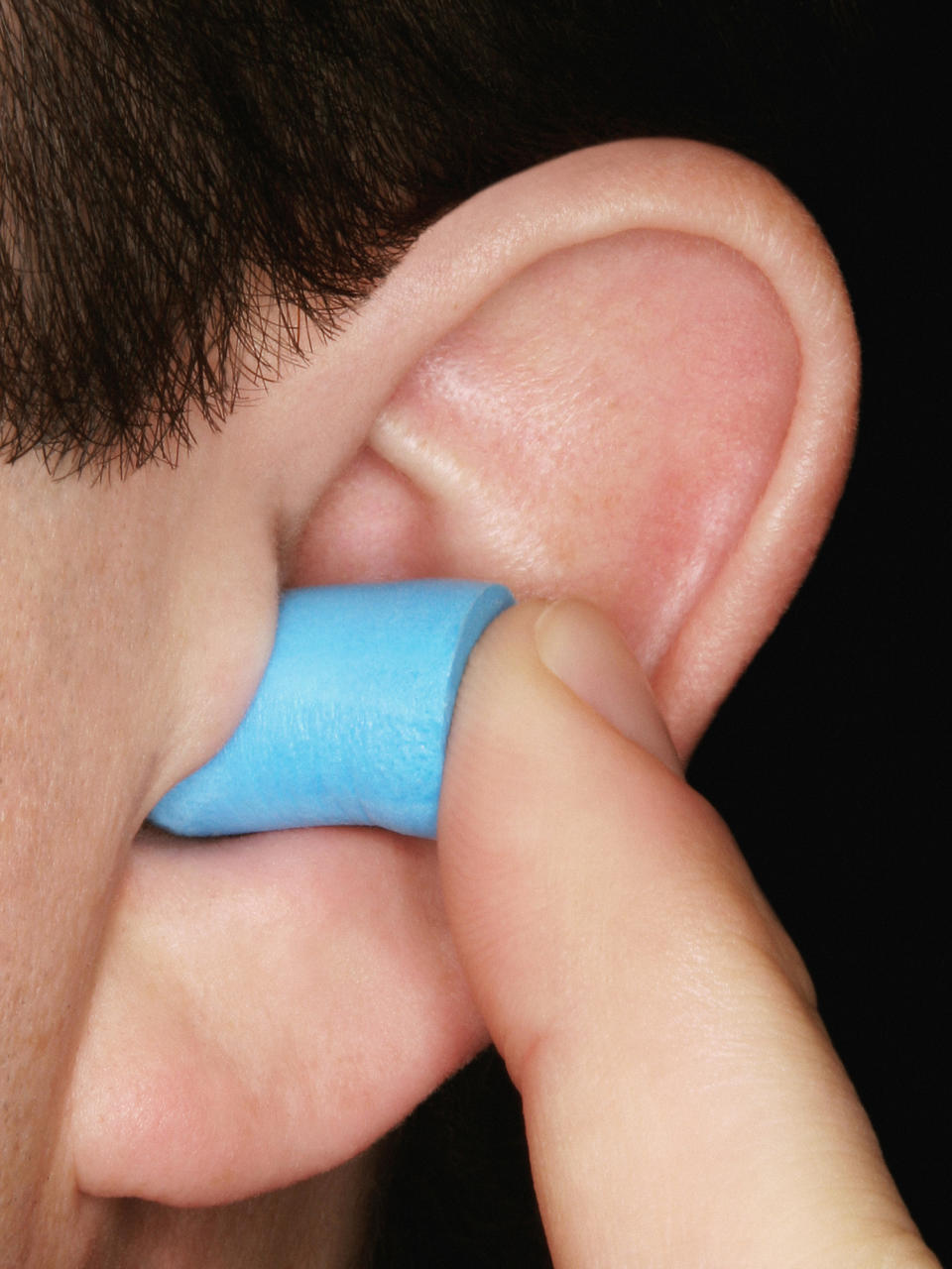 A person gently inserts a blue foam earplug into their ear