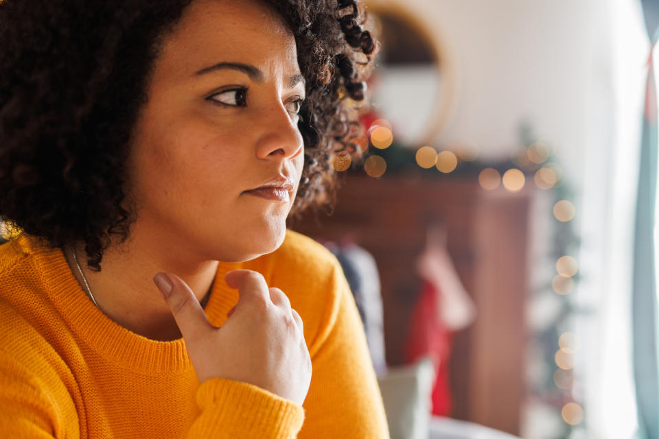 Woman in a yellow sweater looking thoughtful, indoors with soft lighting