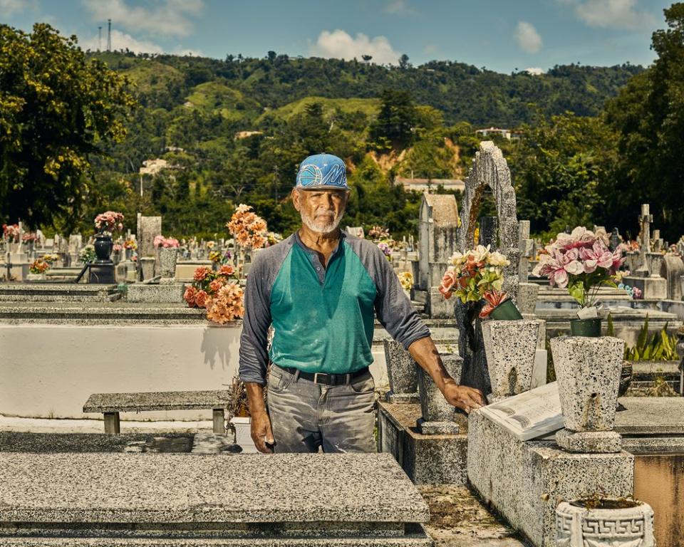 Gravekeeper Tulio Collazo Vega poses by the grave of three elderly sisters who where killed by a landslide the day Maria hit Puerto Rico.