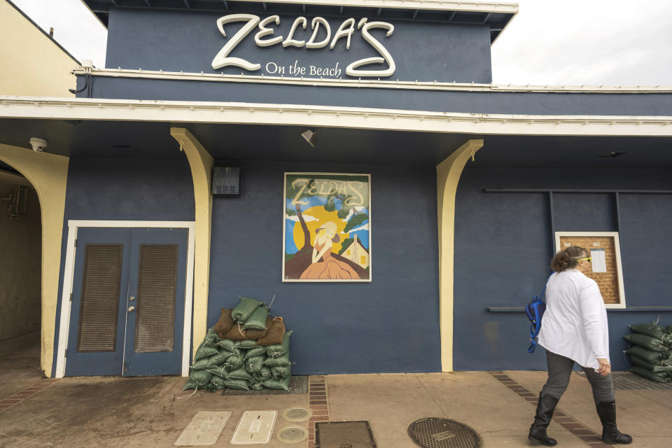 A woman walks by sandbags outside of Zelda's On The Beach Wednesday, Jan. 31, 2024, in Capitola, Calif. The popular village restaurant sustained severe damage from heavy storms in January 2023. An atmospheric river is set to make its way into Northern California, bringing warnings of heavy rain, possible flooding and high winds. (AP Photo/Nic Coury)