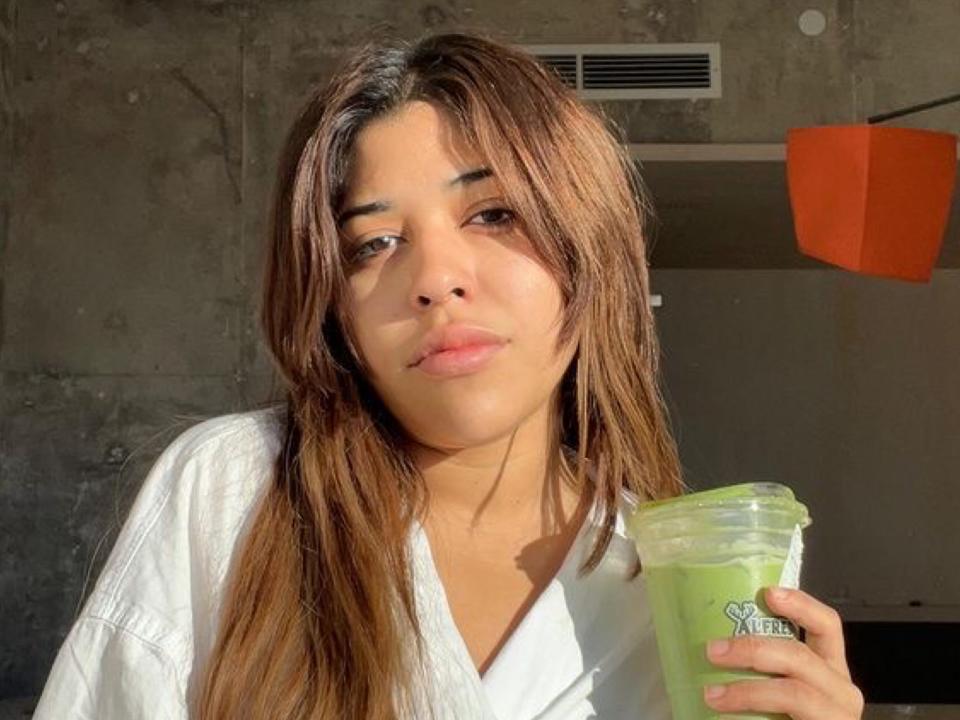 Yoshika Gonzalez, a Latina woman with long brown hair, poses with a green smoothie.