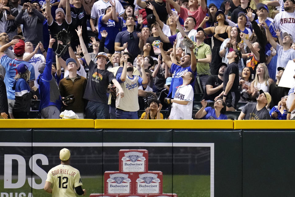 Arizona Diamondbacks left fielder Lourdes Gurriel Jr. (12) looks up as fans reach for the ball on a home run by Los Angeles Dodgers' Chris Taylor during the fourth inning of a baseball game Friday, April 7, 2023, in Phoenix. (AP Photo/Ross D. Franklin)