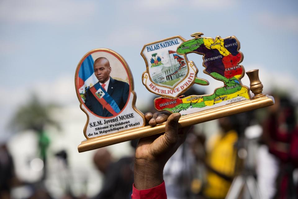 A supporter of Haiti's new President Jovenel Moise holds up his image with Haiti's map and the National Palace, before the earthquake, during his inauguration ceremony in Port-au-Prince, Haiti, Tuesday Feb. 7, 2017. Moise was sworn as president for the next five years after a bruising two-year election cycle, inheriting a struggling economy and a deeply divided society. (AP Photo/Dieu Nalio Chery)