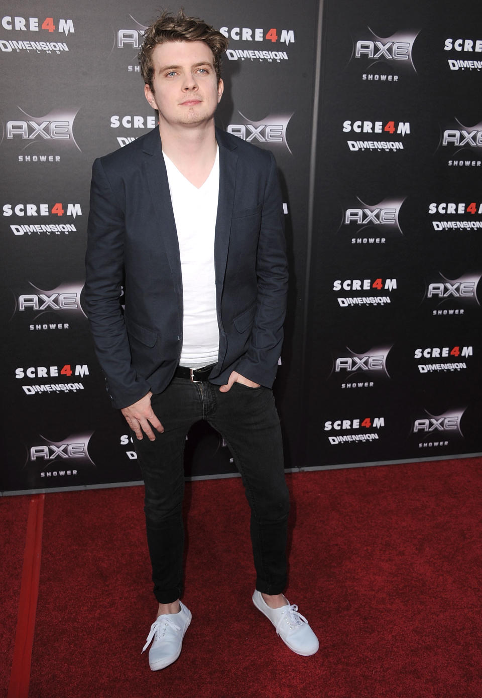 Erik Knudsen in black skinny jeans, a white v-neck shirt, and a black suit jacket