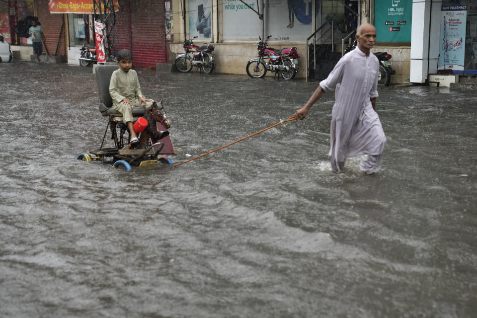 A man pulls a handcart carrying a boy as they wade through a flooded road caused by heavy monsoon rainfall in Lahore, Pakistan, Wednesday, July 5, 2023. Officials say heavy monsoon rains have lashed across Pakistan, killing a number of people. (AP Photo/K.M. Chaudary)