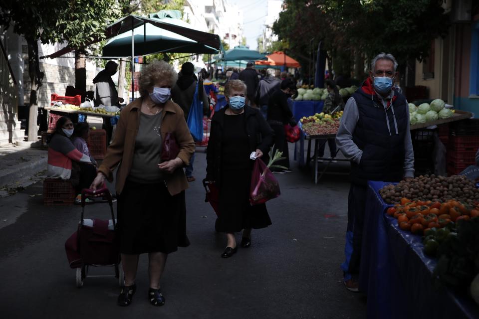 Two women wearing face masks against the spread of coronavirus, pull their trolley baskets at an open-air fruit and vegetable market in Athens, Monday, Nov. 23, 2020. Greece has seen a major resurgence of the virus after the summer, leading to dozens of deaths each day and thousands of new infections. (AP Photo/Thanassis Stavrakis)
