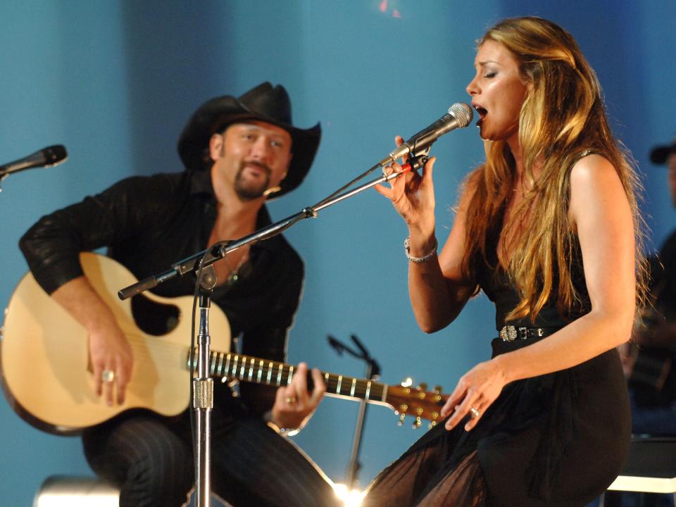 Tim McGraw playing guitar and Faith Hill singing into microphone