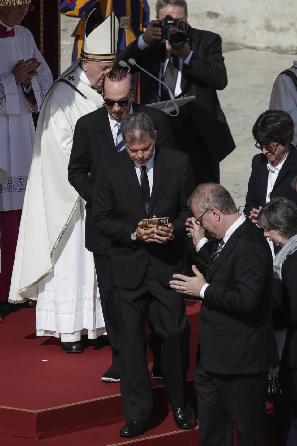 Jose Mauricio Moreira, center, of Salvador, whose healing from glaucoma was considered a miracle that led to the canonization of Dulce Lopes Pontes, leaves after meeting Pope Francis, background left, during a canonization Mass in St. Peter's Square at the Vatican, Sunday, Oct. 13, 2019. Francis presided over Mass on Sunday in a packed St. Peter's Square to declare Cardinal John Henry Newman and four women saints. (AP Photo/Alessandra Tarantino)