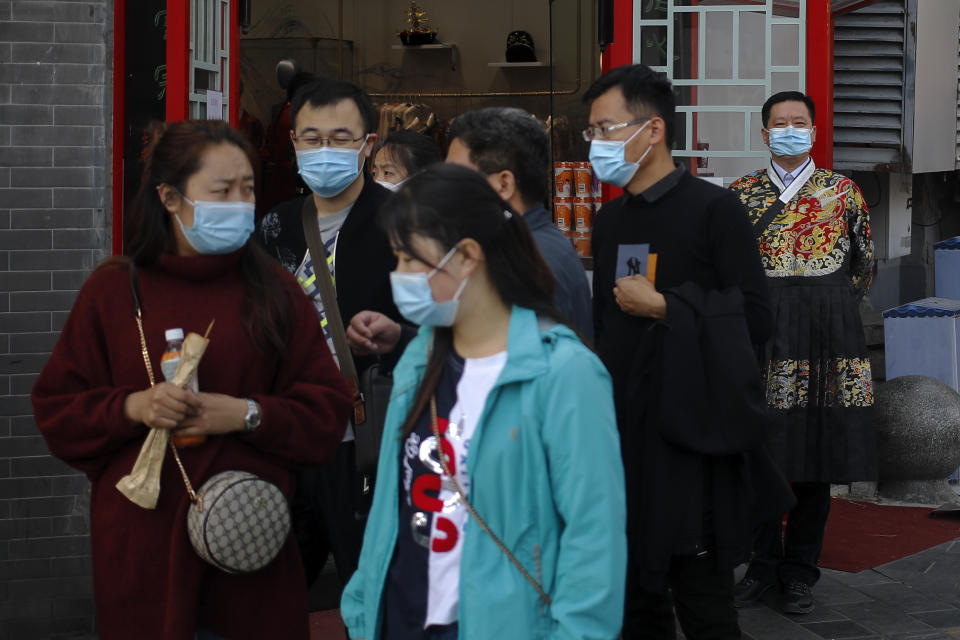 A worker wearing a face mask to help curb the spread of the coronavirus, right, stands watch masked tourists walk by his souvenir shop in Beijing, Sunday, Oct. 25, 2020. With the outbreak of COVID-19 largely under control within China's borders, the routines of normal daily life have begun to return for its citizens. (AP Photo/Andy Wong)