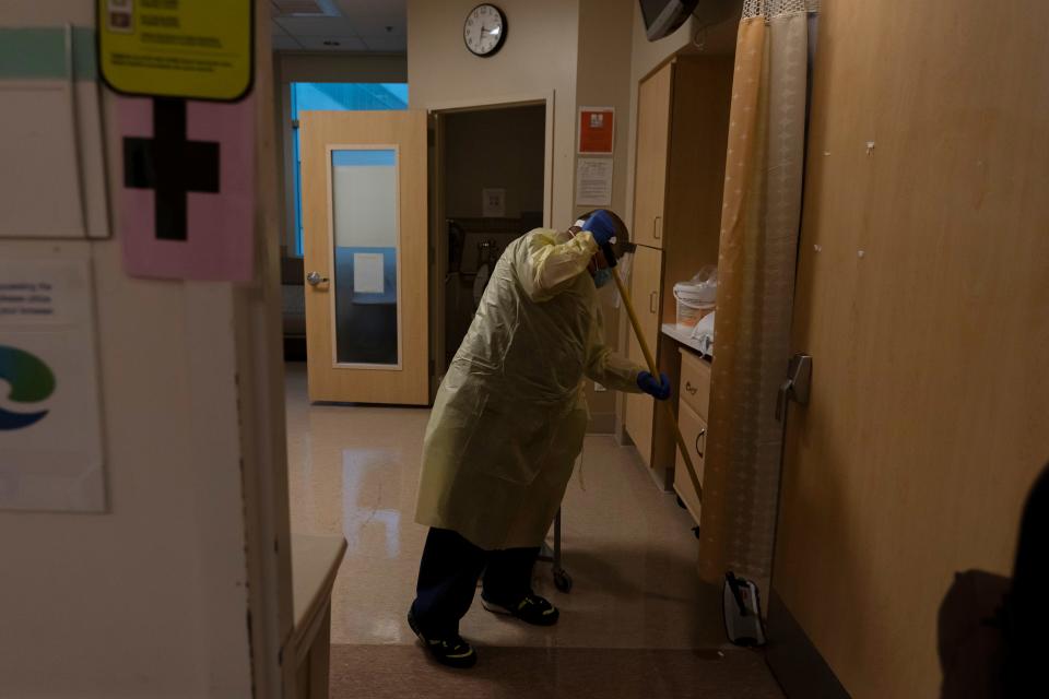 FILE - Environmental technician Gerardo Velazquez cleans a room after a COVID-19 patient was transferred to an intensive care unit at Providence Holy Cross Medical Center in Los Angeles, Monday, Dec. 13, 2021. The worldwide surge in coronavirus cases driven by the new omicron variant is the latest blow to already strained hospitals, nursing homes, police departments and supermarkets struggling to maintain a full contingent of nurses, police officers and other essential workers as the pandemic enters its third year.  (AP Photo/Jae C. Hong, File)