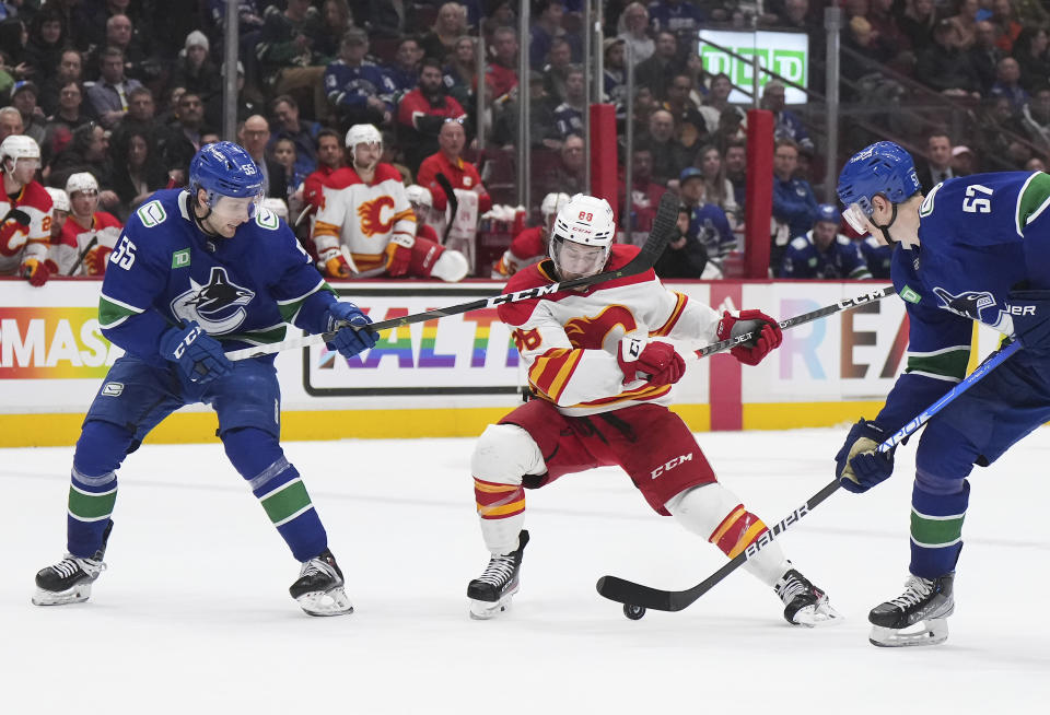 Vancouver Canucks' Guillaume Brisebois (55) hits Calgary Flames' Andrew Mangiapane (88) on the face with his stick as Canucks' Tyler Myers (57) watches during the second period of an NHL hockey game Friday, March 31, 2023, in Vancouver, British Columbia. (Darryl Dyck/The Canadian Press via AP)