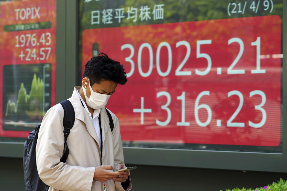 A man wearing a protective mask walks in front of an electronic stock board showing Japan's Nikkei 225 index at a securities firm in Tokyo Friday, April 9, 2021. (AP Photo/Eugene Hoshiko)