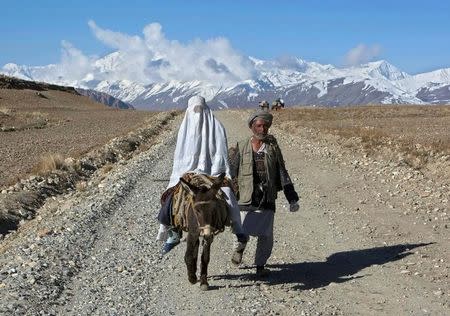 An Afghan woman, wearing a burqa, rides on a donkey alongside her husband in the Ishkashim district of Badakhshan province, north east of Kabul April 24, 2008. REUTERS/Ahmad Masood/File Photo