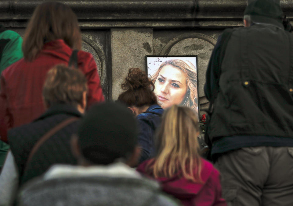 A portrait of slain television reporter Viktoria Marinova is placed on the Liberty Monument, as people wait to place flowers and candles during a vigil in Ruse, Bulgaria, Monday, Oct. 8, 2018. Bulgarian police are investigating the rape, beating and slaying of a female television reporter whose body was dumped near the Danube River after she reported on the possible misuse of European Union funds in Bulgaria. Authorities discovered the body of 30-year-old Viktoria Marinova on Saturday in the northern town of Ruse near the Romanian border. One Bulgarian media site demanded an EU investigation, fearing that Bulgarian officials were complicit in the corruption. (AP Photo/Vadim Ghirda)