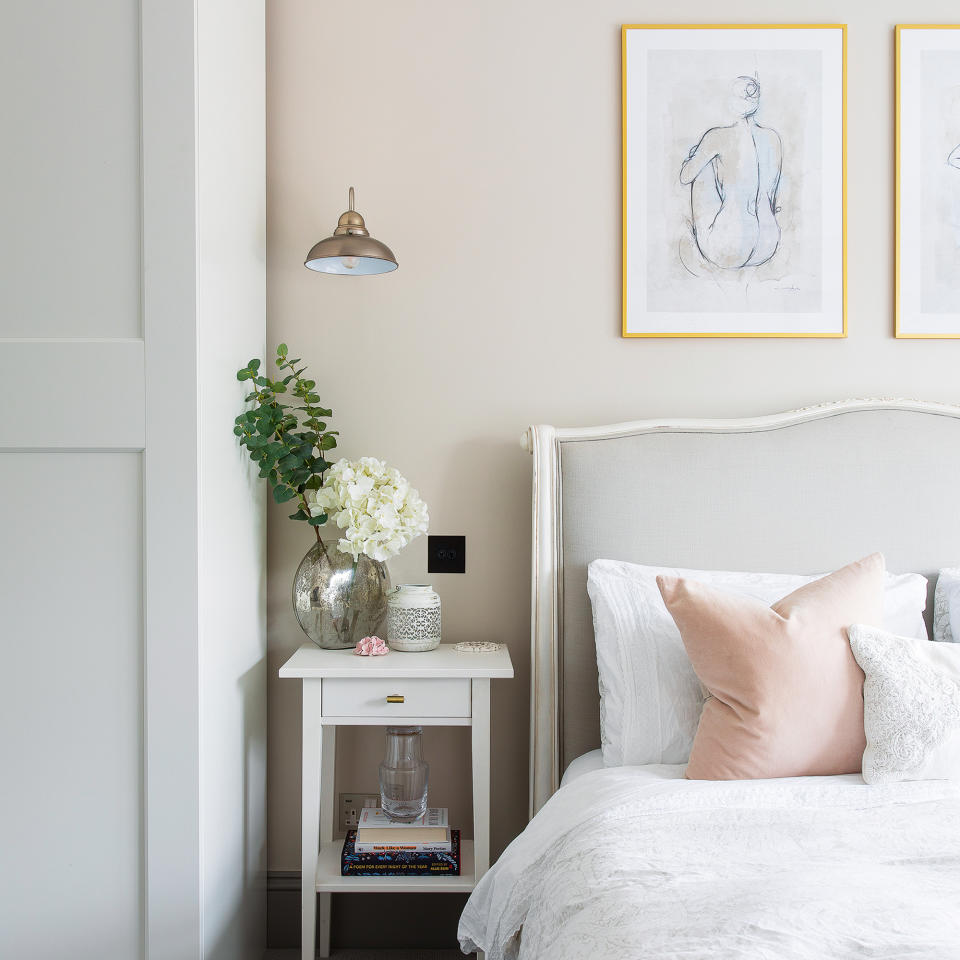 Neutral bedroom with upholstered headboard, white bedside table, ceiling light and artwork