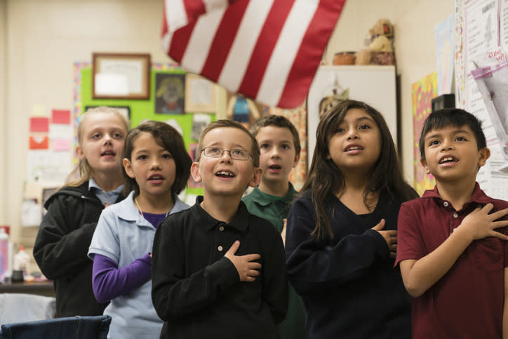 Kids doing the pledge of allegiance to the U.S. flag in a classroom