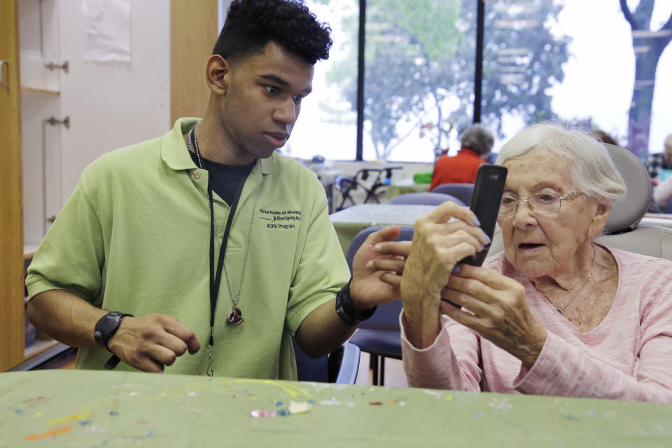 Kevin Perez, 19, in the HOPE program at the Hebrew Home at Riverdale, in New York, assists resident Belle Bishop, age 93, with her mobile phone in the art studio Thursday, May 25, 2017. (AP Photo/Richard Drew)