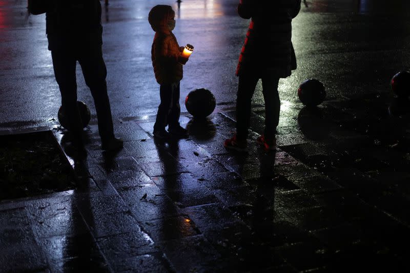 A boy holding a lit candle looks at his mother while they attend an event ment to commemorate the 65 victims of the Colectiv fire