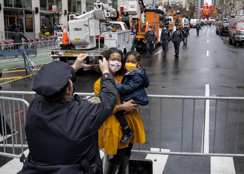 A New York City police officer takes a photo for a passerby as the modified Macy's Thanksgiving Day Parade moves along a few blocks away in the background, in New York, Thursday, Nov. 26, 2020. Due to the pandemic, crowds of onlookers were not allowed to attend the annual parade. (AP Photo/Craig Ruttle)