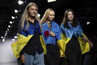 Designers Ksenia Schnaider, from left, Nadya Dzyak, and Elena Reva walk the catwalk wearing Ukrainian flags on Tuesday, Sept. 19, 2023 in London. For Ksenia Schaider and other Ukrainian designers, the fashion show must go on, despite the war in their country or precisely because of it. Schaider may have fled to the U.K. as a refugee, but her team still makes every garment in Kiev, often under incessant air raid sirens and lengthy power cuts. (Scott Garfitt/Invision/AP)