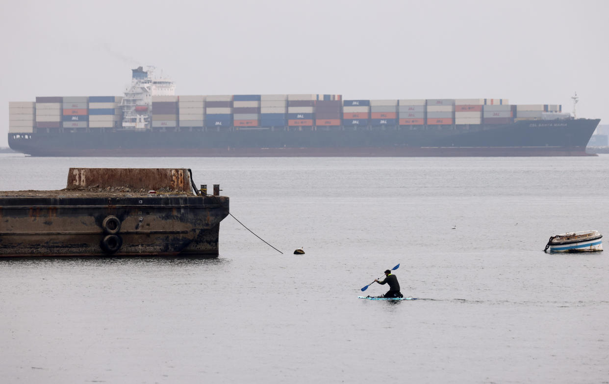 LONG BEACH, CALIFORNIA - DECEMBER 02: A person paddle boards near shipping containers stacked on a container ship at the Port of Long Beach on December 2, 2021 in Long Beach, California. The Ports of Los Angeles and Long Beach have delayed a plan for a fourth time to charge shippers fees for container storage as a backlog of aging cargo at the ports has decreased 37 percent since last month.  (Photo by Mario Tama/Getty Images)