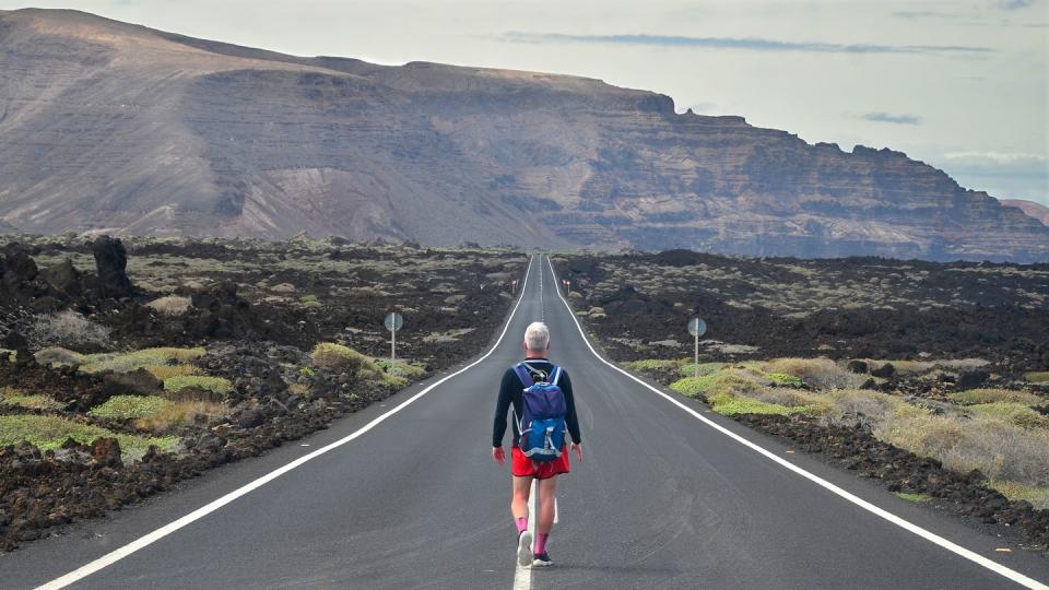 lonely oung man walking on an endless road in a volcanic landscape in lanzarote, canary islands