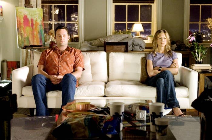 Vince Vaughn and Jennifer Aniston sit on a couch with neutral expressions in a living room setting at night