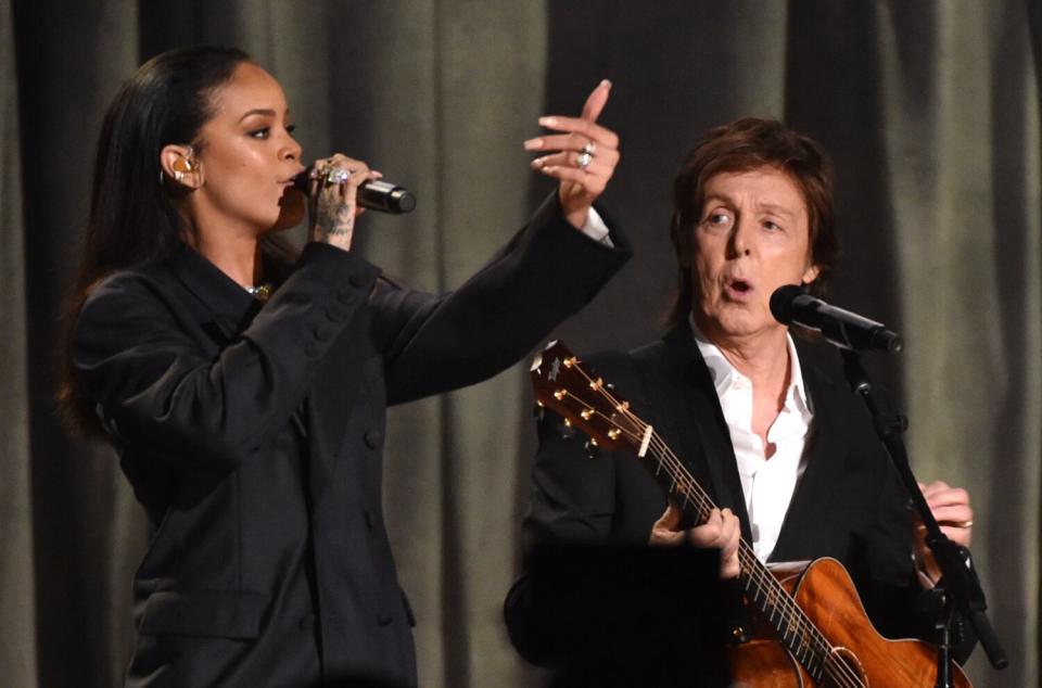 A woman in black sings into a microphone while a man plays guitar and sings