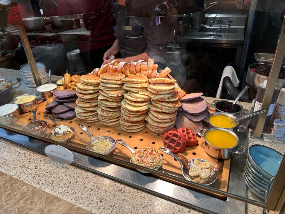 Stacks of funfetti pancakes surrounded by sprinkles, butters, syrups, and waffles at Bacchanal buffet