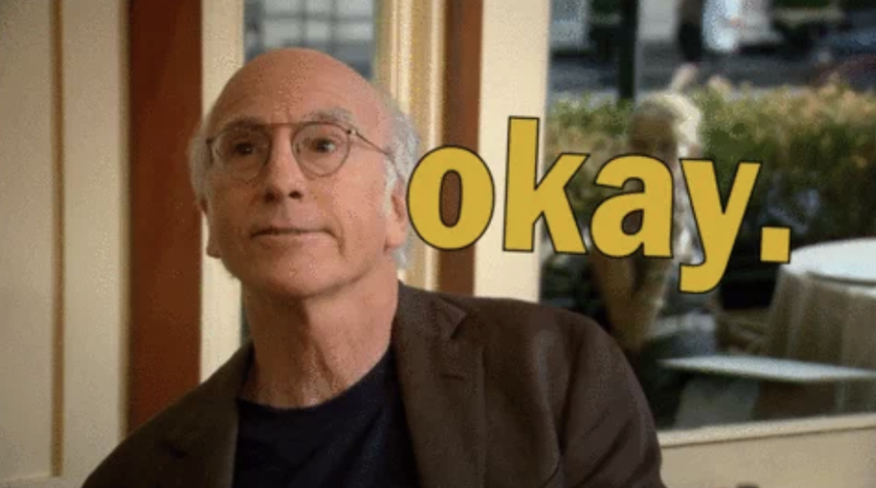 Larry David wearing glasses and a suit, with "okay" in large yellow text next to him