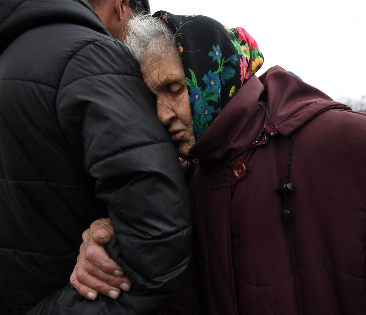 A man comforts an elderly woman in a headscarf as families search for missing loved ones in Bucha.