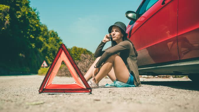 Woman on the side of the road with broken down car, calling for assistance.