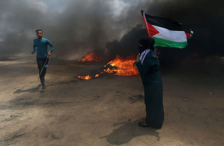 A woman holds a Palestinian flag as a demonstrator runs during a protest against U.S. embassy move to Jerusalem and ahead of the 70th anniversary of Nakba, at the Israel-Gaza border in the southern Gaza Strip May 14, 2018. REUTERS/Ibraheem Abu Mustafa