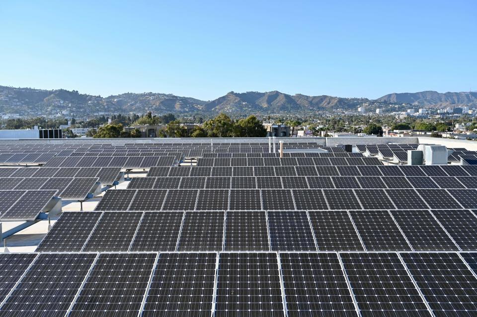 As many as a dozen arrays of solar panels stretch out on the roof of a building, with a backdrop of mountains.