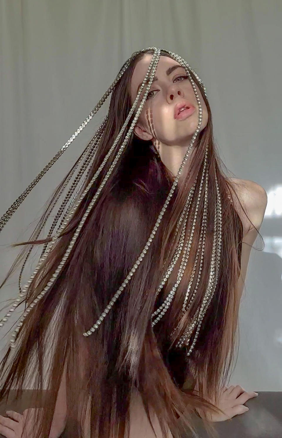 Close-up photo of disabled model Cherie Louise wearing a black leotard with silver chains hanging through her long brown hair. Photo: Instagram/cherie.louise (supplied).