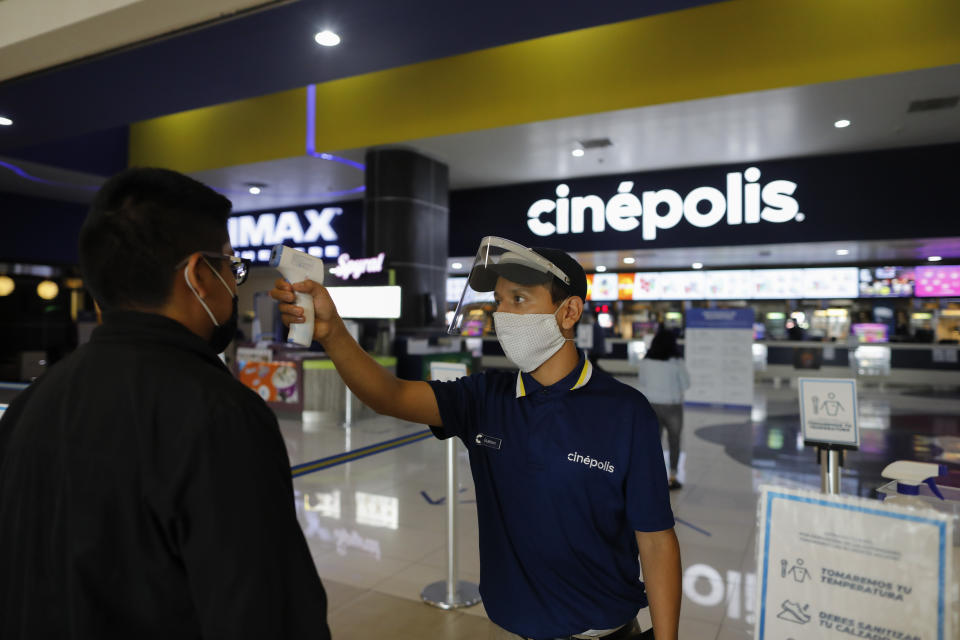 El empleado Gustavo Angel Oropeza Alvarez, de 21 años, mide la temperatura de un asistente a la sucursal de cines de la cadena Cinépolis en el centro comercial Forum Buenavista de la Ciudad de México el miércoles 12 de agosto de 2020. Después de estar cerrados casi cinco meses los cines reabrieron en la capital a 30% de capacidad.(Foto AP/Rebecca Blackwell)