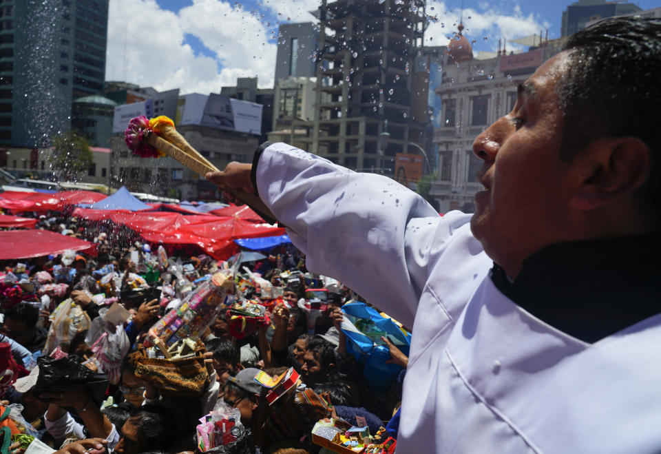 Un cura echa agua bendita para bendecir los objetos en miniatura y billetes falsos durante la feria anual de Alasita en el centro de La Paz, Bolivia, el miércoles 24 de enero de 2024. En el día de inauguración de la feria se ofrecen réplicas en miniatura de las cosas que las personas anhelan o desean, como casas, vehículos o salud, para que se conviertan en realidad. Alasita es una palabra aymara que significa "cómprame". (AP Foto/Juan Karita)