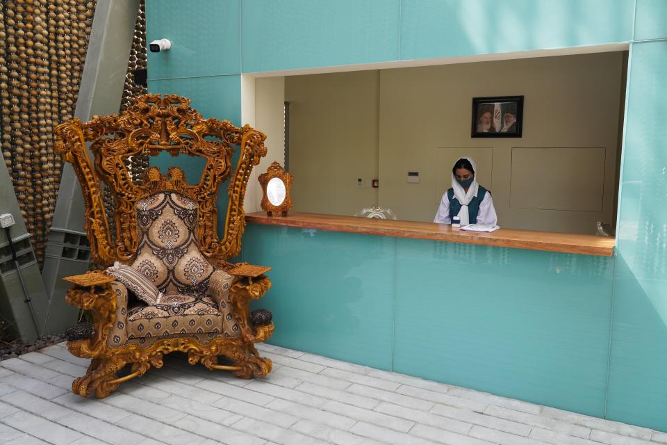 A woman prepares to greet visitors to Iran's pavilion at Expo 2020 in Dubai, United Arab Emirates, Saturday, Oct. 2, 2021. Dubai has gambled billions to make the gleaming, built-from-scratch Expo village a triumphant tourist attraction and symbol of the United Arab Emirates itself — a feast for the eyes devoid of politics and built on the promise of globalization. But even as nations use their pavilions for benign infomercials, the political turbulence of the wider world somehow manages to intrude. The two men in the photo behind her are Iran's late Supreme Leader Ayatollah Ruhollah Khomeini, left, and current Supreme Leader Ayatollah Ali Khamenei. (AP Photo/Jon Gambrell)