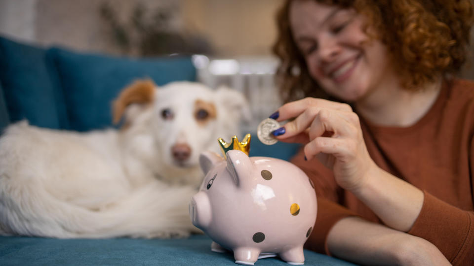 woman paying money into piggy bank with dog watching on