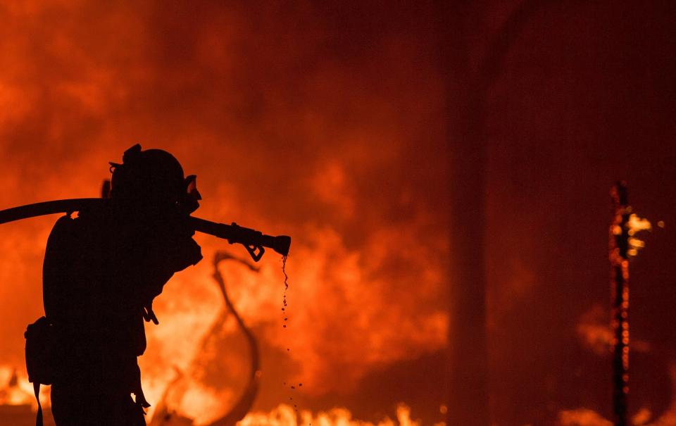 A firefighter pulls a hose in front of a burning house in the Napa wine region of California on Oct. 9, 2017. (Photo: JOSH EDELSON/AFP/Getty Images)
