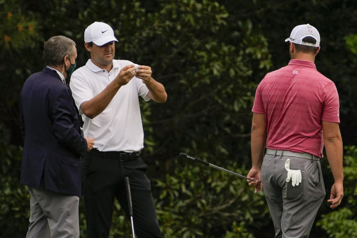 Xander Schauffele examines a ball with a rules official as Jon Rahm, of Spain, watches on the fifth hole during the final round of the Masters golf tournament on Sunday, April 11, 2021, in Augusta, Ga. (AP Photo/Gregory Bull)