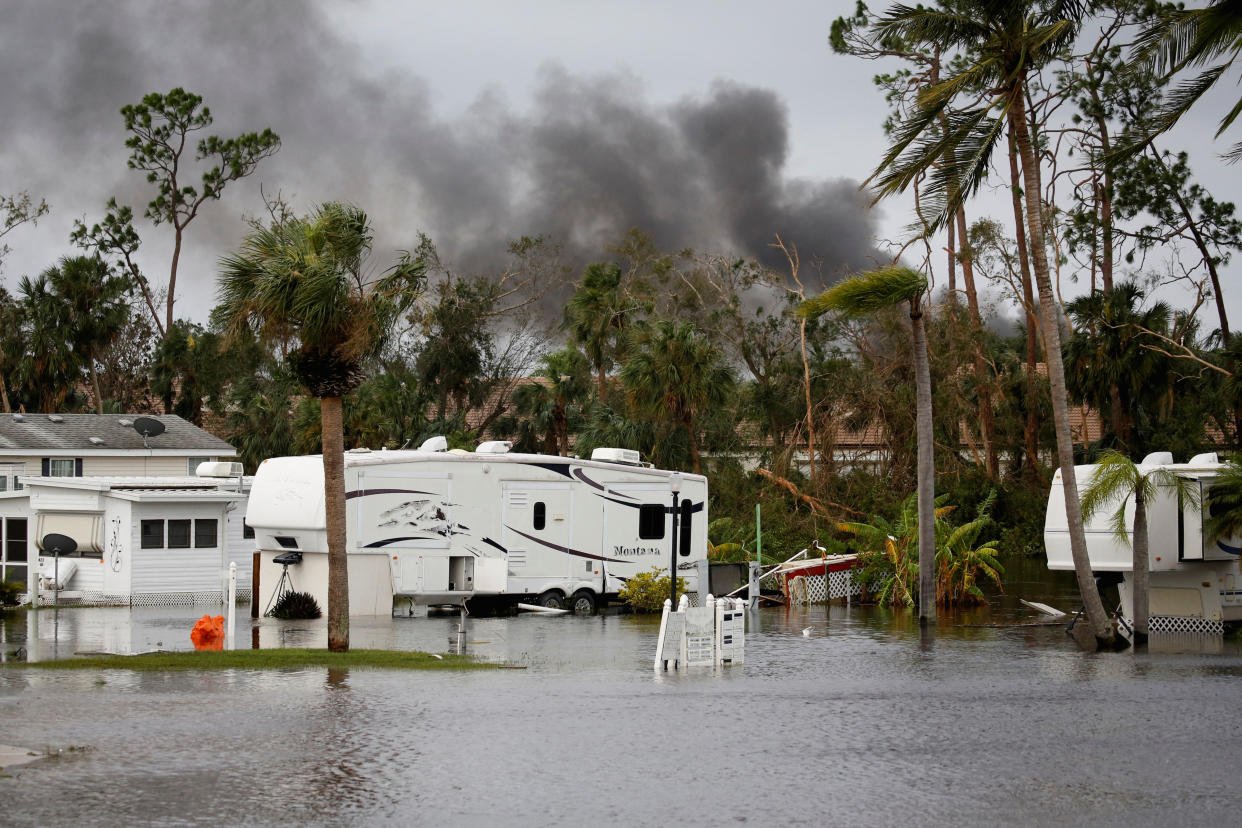 Motor homes in a flooded area with billowing smoke rising in the background.