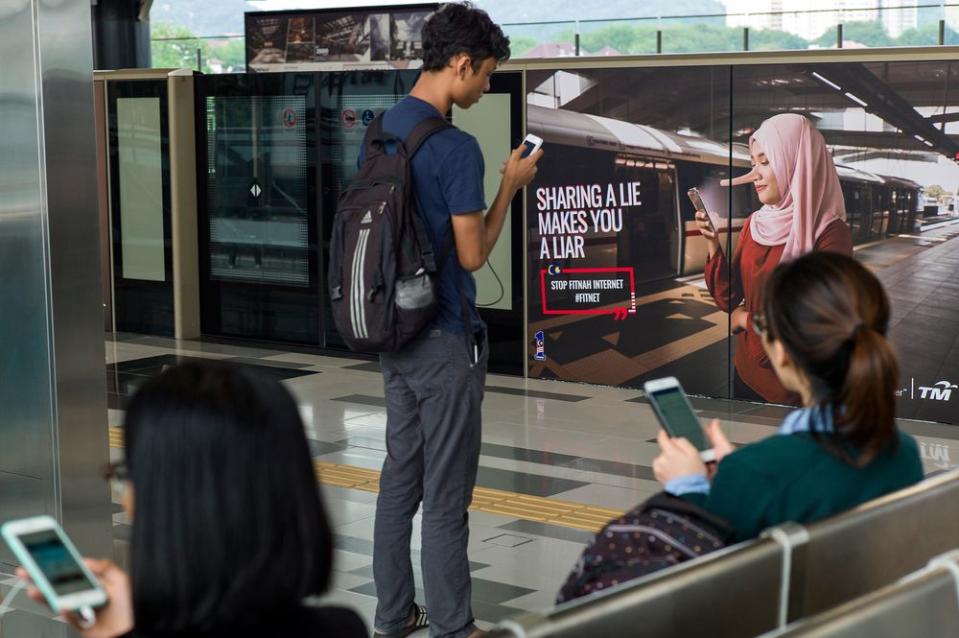 Commuters use their smartphones near an advertisement that reads