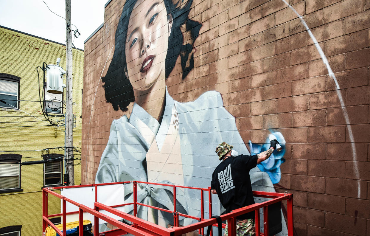 Los Angeles based artist Chris Shim, 29, aka "Royyal Dog" works on a mural of wife Areum, Tuesday, Sept. 17, 2019, in the alley behind Traction on the 600 block of E. Michigan Avenue.  "I hope she likes it," he said.  Shim and his wife moved to the U.S. from S. Korea four months ago.  "It's been our dream to live and work here," he says. His large scale photorealistic work covers walls throughout the world, and now in Lansing as one of eleven murals being created as part of Lansing's Below the Stacks mural festival.