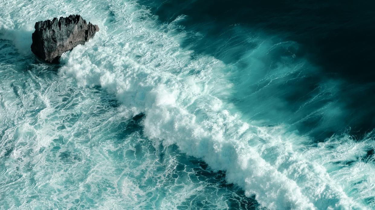  An aerial view of waves breaking on a rock and water foaming. 