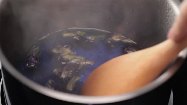 Boiling blue butterfly pea flower and stirring with a wooden spatula