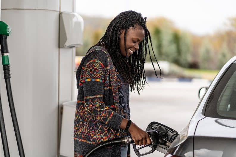 Person smiling while pumping fuel into the gas tank of a vehicle.