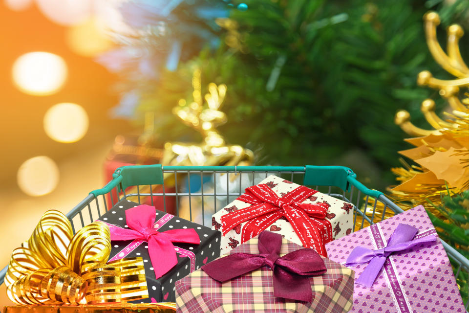 Christmas gifts and presents in shopping trolley with christmas decorations and blurred lights on christmas tree background. 