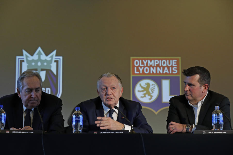 Jean-Michel Aulas, center, owner and president of the French soccer team Olympique Lyonnais, speaks as Bill Predmore, right, former owner of the National Women's Soccer League Reign FC team, and OL Groupe's Gerard Houllier, left, look on, Thursday, Dec. 19, 2019, at a news conference in Tacoma, Wash. OL Groupe, the parent company of Olympique Lyonnais, is buying Reign FC, of the in a transaction expected to close in January 2020. Reign FC will continue to play its home games at Cheney Stadium, the venue it shares with the Triple-A minor league baseball team the Tacoma Rainiers. (AP Photo/Ted S. Warren)